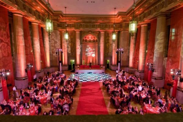 Elegant ballroom filled with guests at round tables, featuring red decor and a checkered dance floor under ambient lighting.