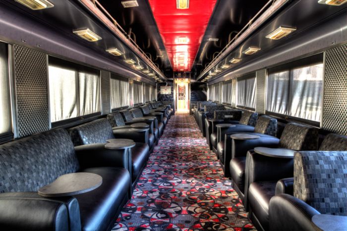 Interior of a train car featuring rows of black leather seating and patterned carpet along with large windows.