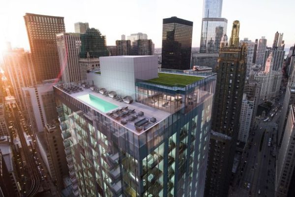 Rooftop view of a modern skyscraper with a pool and lounging area, overlooking a bustling cityscape at sunset.