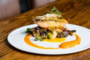 Grilled salmon atop a bed of sautéed vegetables with a drizzle of vibrant orange sauce on a white plate.