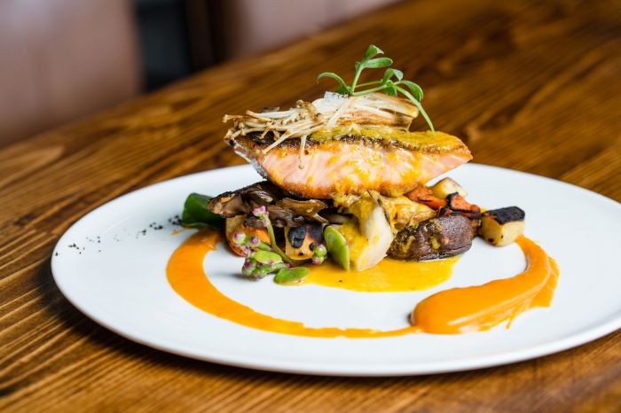 Grilled salmon atop a bed of sautéed vegetables with a drizzle of vibrant orange sauce on a white plate.
