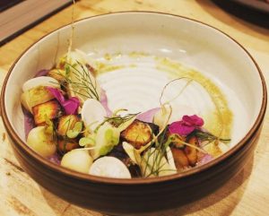 A beautifully presented dish featuring grilled ingredients, edible flowers, and vibrant garnishes in a round bowl.