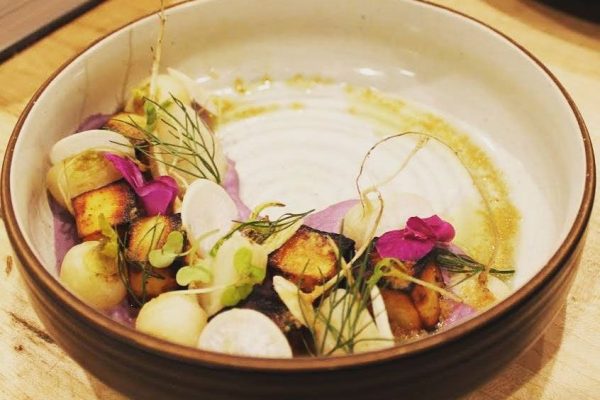 A beautifully presented dish featuring grilled ingredients, edible flowers, and vibrant garnishes in a round bowl.