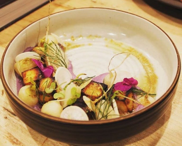 A beautifully presented dish featuring grilled ingredients, edible flowers, and vibrant garnishes in a round bowl.