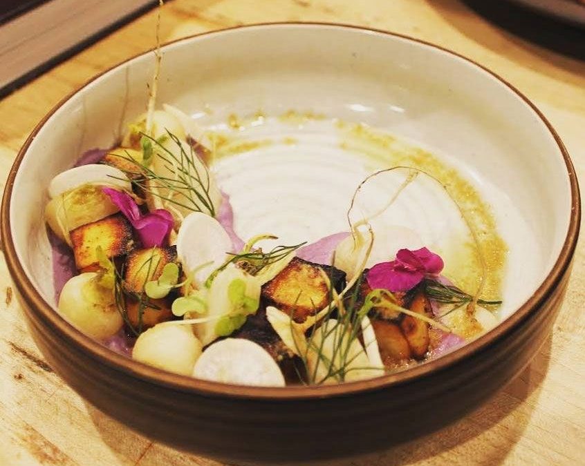 A beautifully presented dish featuring grilled ingredients, edible flowers, and vibrant garnishes in a round bowl.