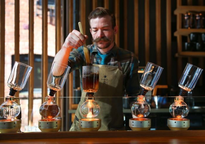 Barista using a siphon coffee maker to brew coffee, with multiple glass chambers in a stylish café setting.