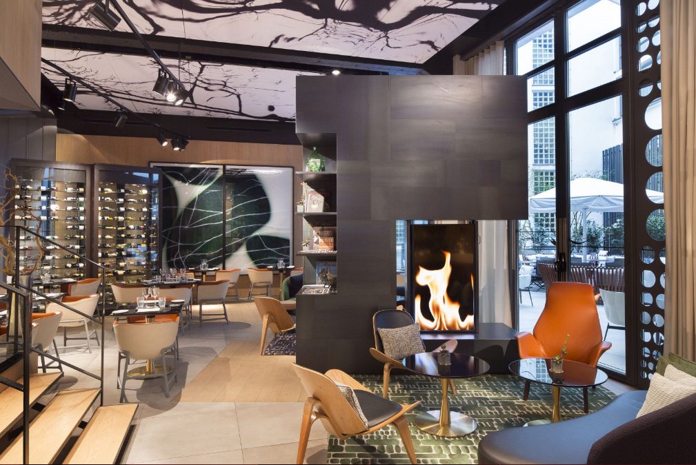 Modern dining area featuring stylish furniture, a wine display, a fireplace, and large windows overlooking an outdoor space.