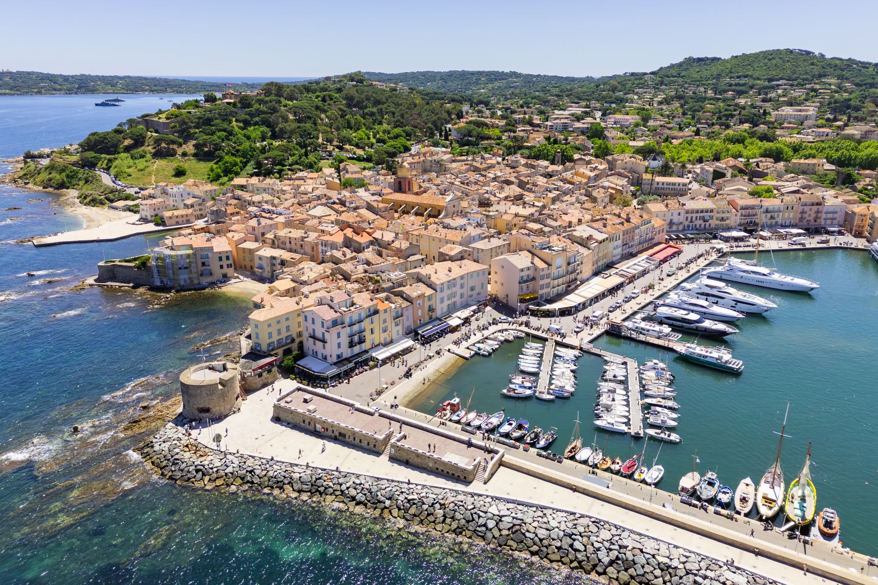 Aerial view of the scenic coastline and vibrant harbor of Saint-Tropez, showcasing charming architecture and luxurious yachts.