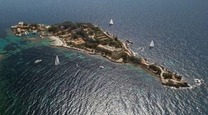 Aerial view of a picturesque island in the sea featuring lush greenery, sandy beaches, and sailing boats.