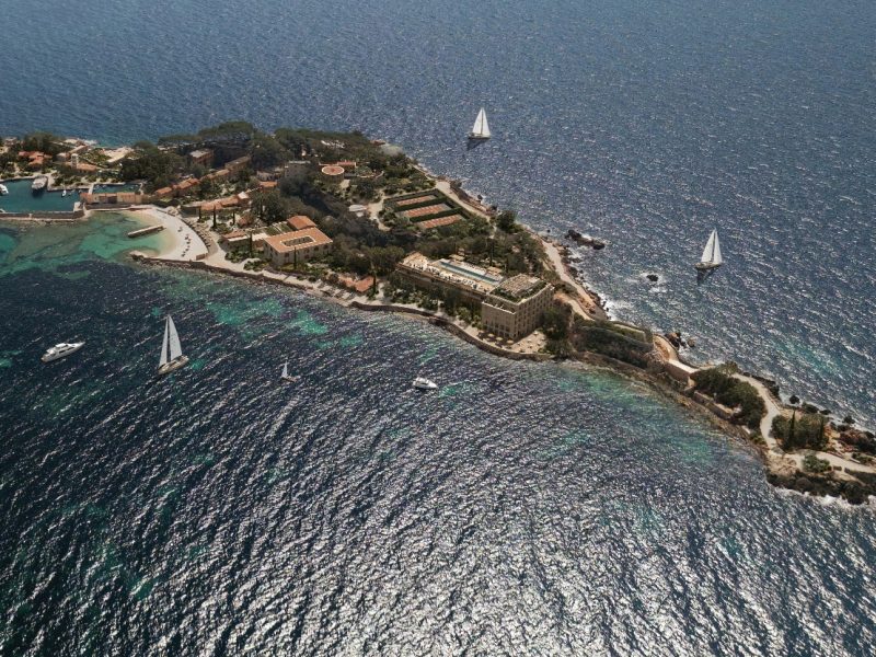 Aerial view of a picturesque island in the sea featuring lush greenery, sandy beaches, and sailing boats.