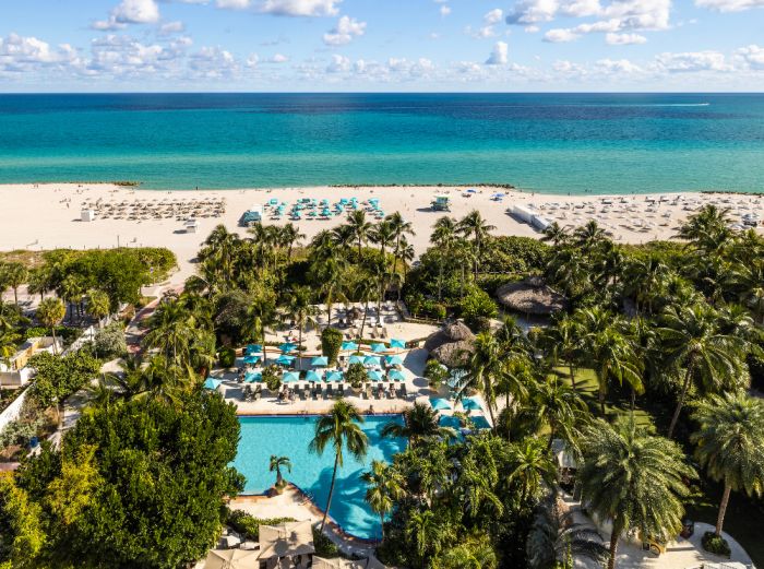 Aerial view of The Palms Hotel & Spa with a pool area, palm trees, and ocean beach in the background.