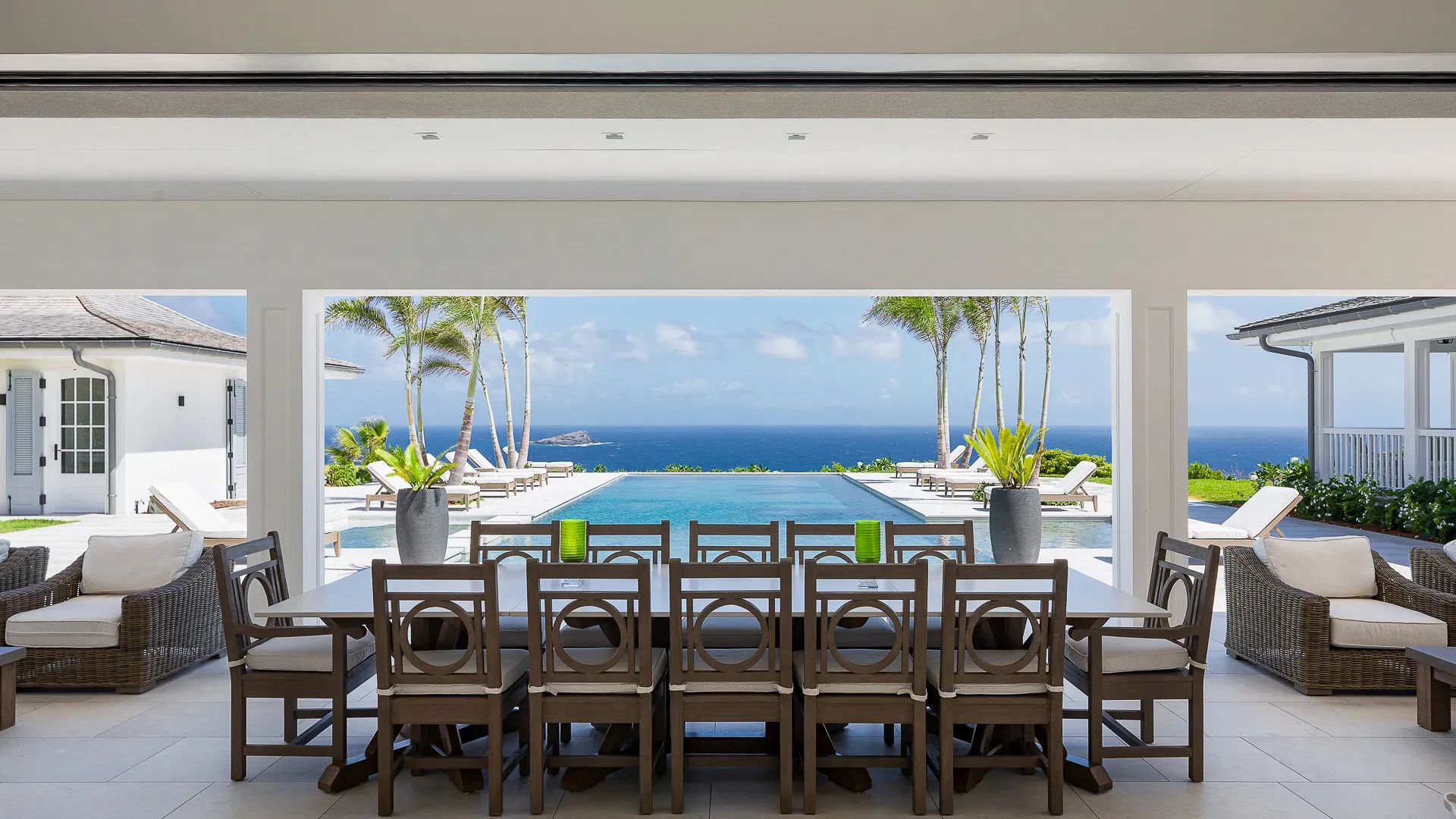 Spacious dining area with wooden chairs overlooks a luxurious pool and ocean view in a stylish villa setting.