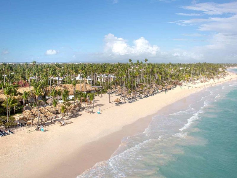 Aerial view of Grand Palladium Bavaro Suites Resort and Spa, showcasing palm trees and a sandy beach along the turquoise ocean.