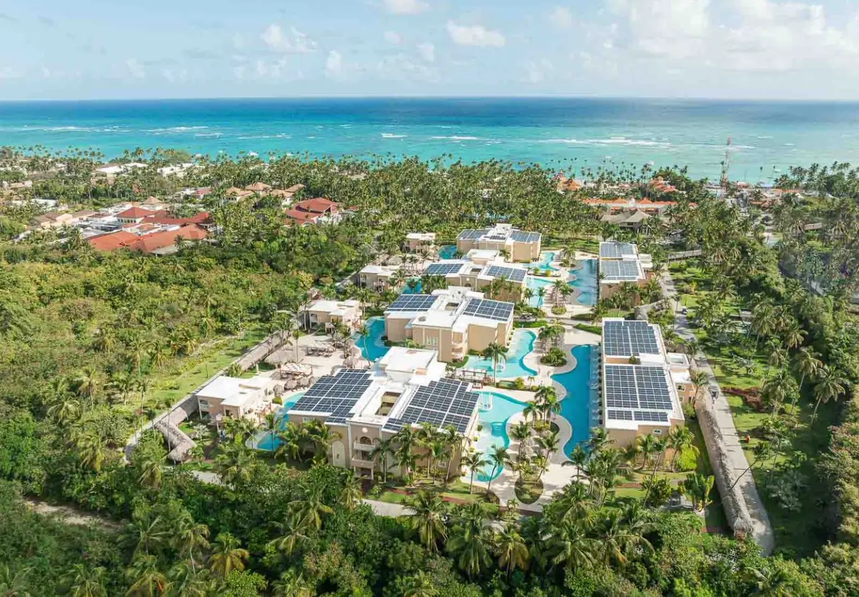 Aerial view of a luxurious resort with solar panels, pools, and palm trees, overlooking the ocean in the Dominican Republic.
