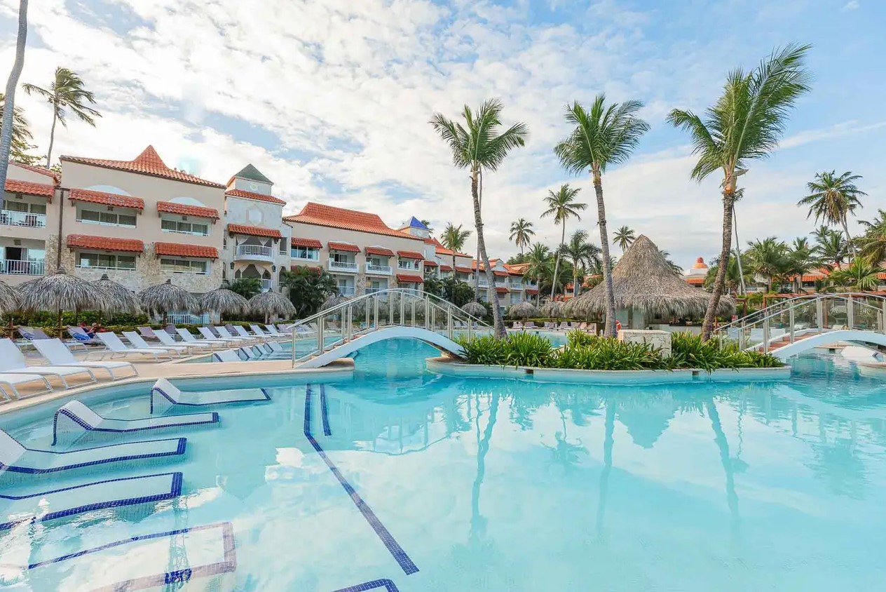 Luxury hotel pool area featuring loungers, palm trees, and thatched-roof cabanas at TRS Turquesa in the Dominican Republic.