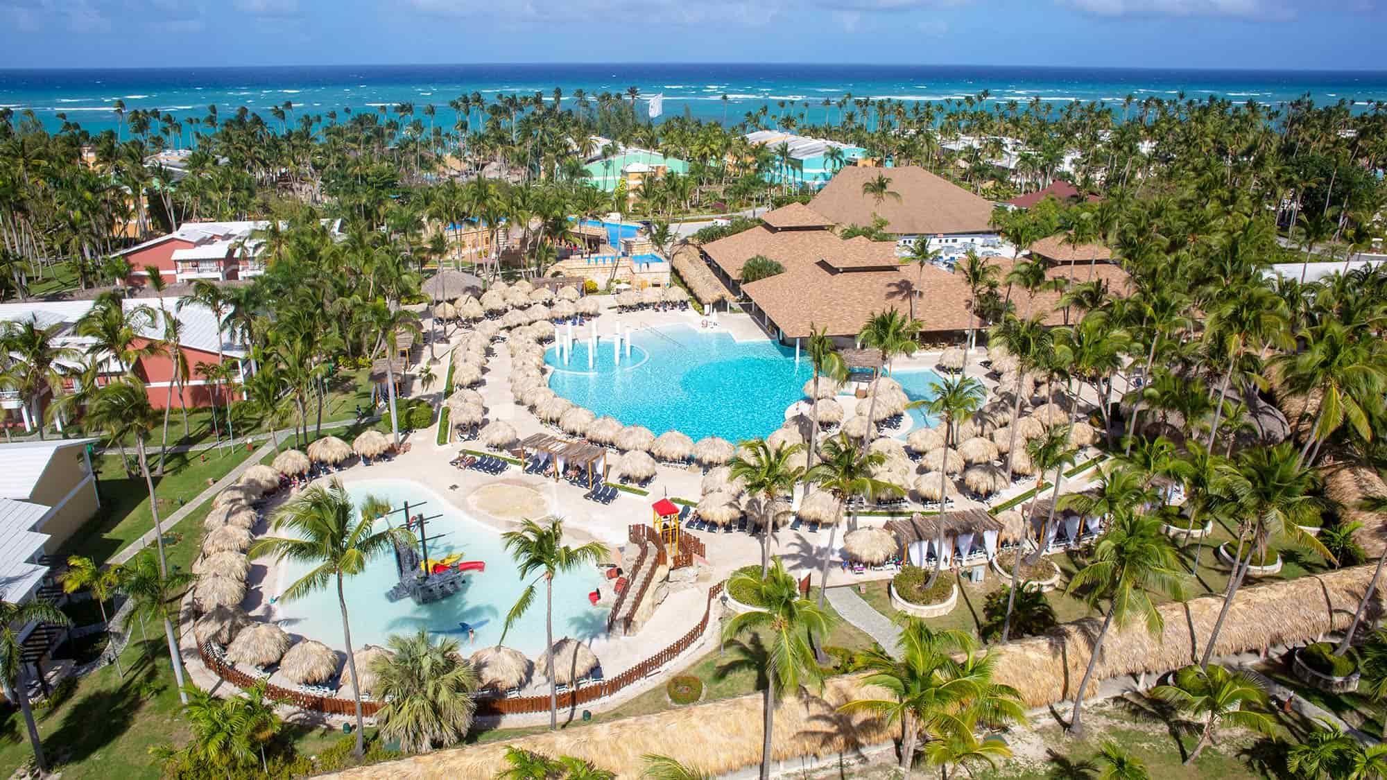 Aerial view of Grand Palladium Punta Cana Resort with pools, palm trees, and the beach in the background.