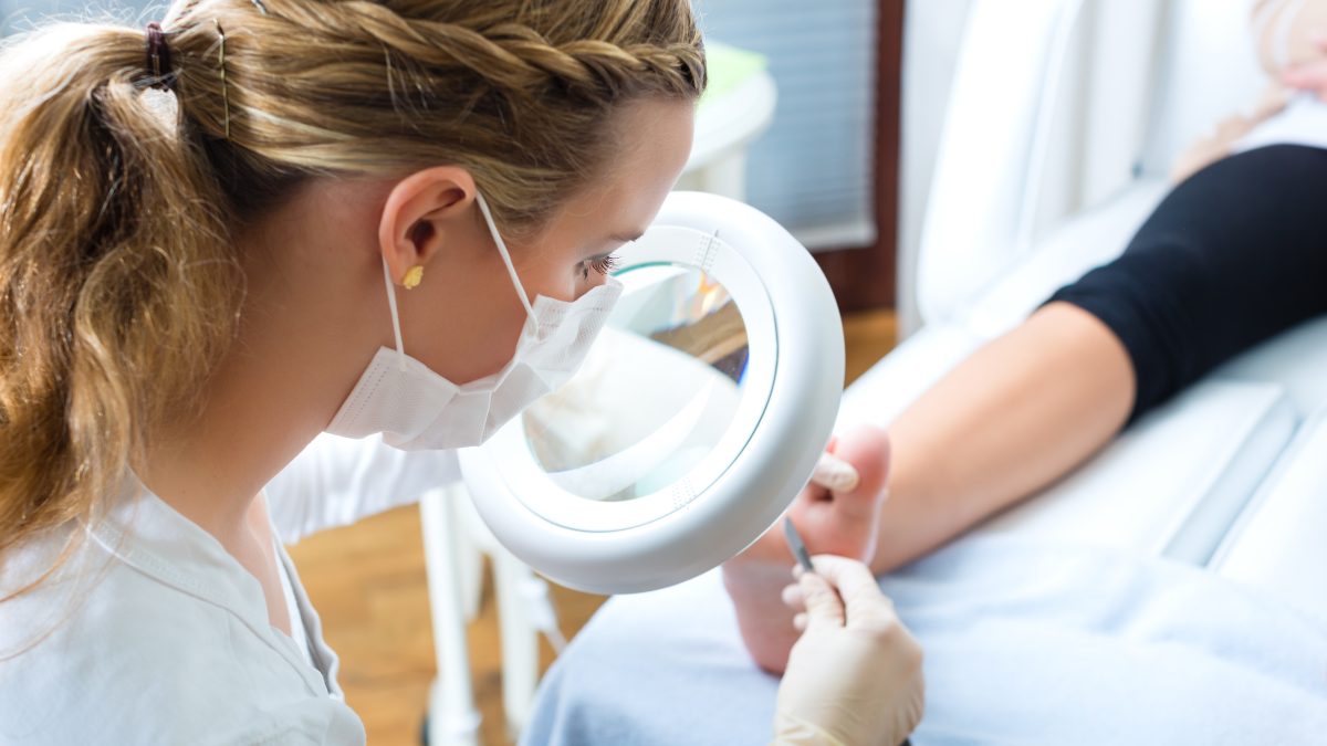 A professional examines a client's foot using a magnifying lamp during a medical pedicure session.