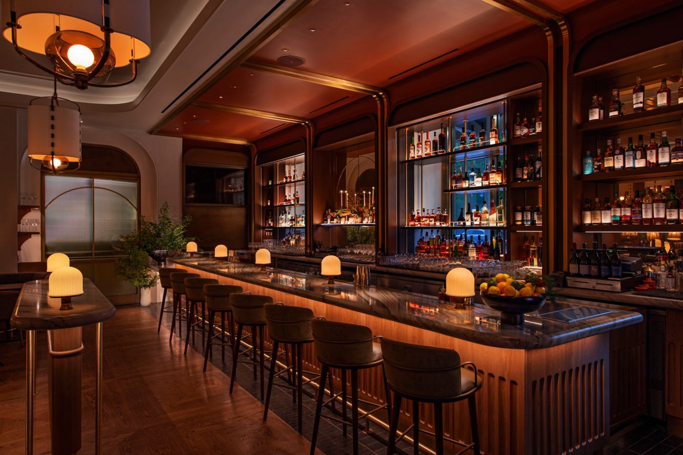 Stylish bar area with illuminated fixtures, rich wood finishes, and shelves lined with an array of spirits and cocktails.