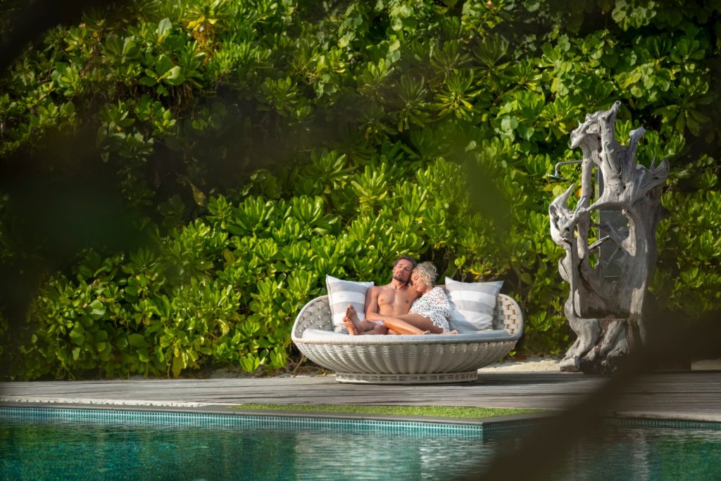 Couple relaxing together on a private lounge by the pool surrounded by lush greenery in the Maldives.
