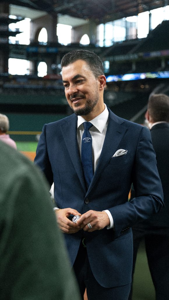 Jason of Beverly Hills wears a stylish suit and holds a championship ring while interacting with others at an event.