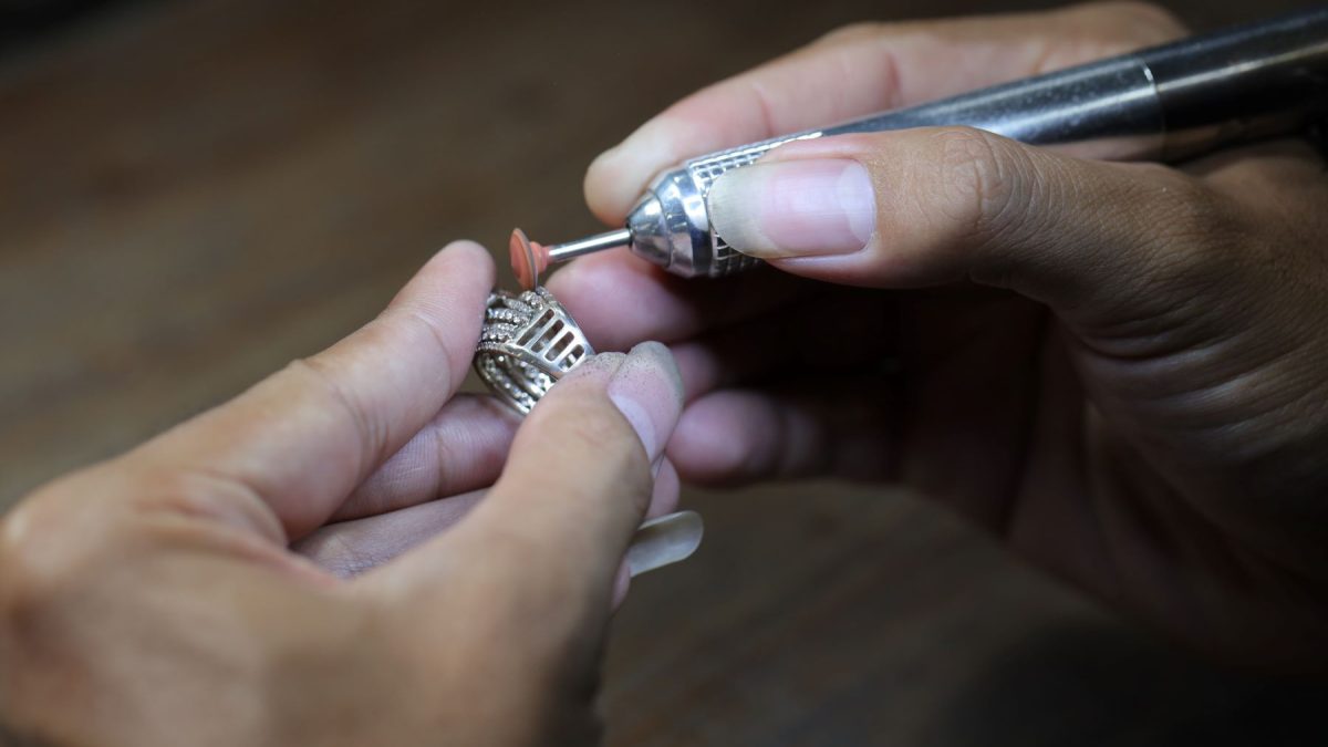 A jeweler uses a tool to work on a silver necklace detailing fine craftsmanship and intricate design.