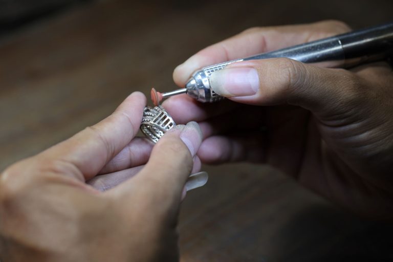 A jeweler uses a tool to work on a silver necklace detailing fine craftsmanship and intricate design.
