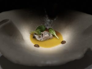 Delicate dish featuring an oyster on a bed of vibrant sauce, garnished with microgreens and small accents.