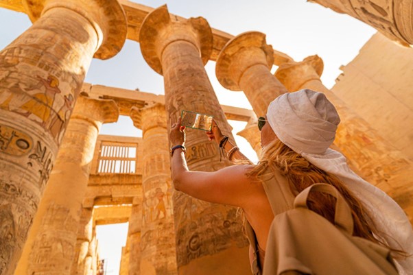 A visitor takes a photo of ancient columns adorned with hieroglyphics inside a historic Egyptian temple.