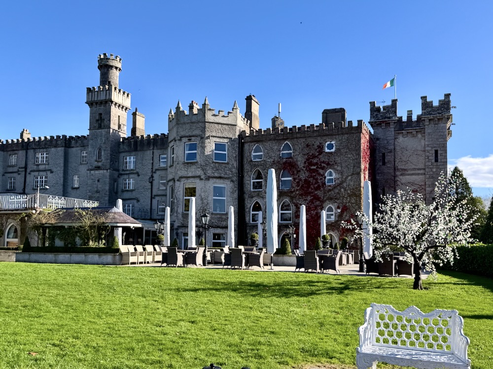 Cabra Castle in Ireland features historic architecture, lush green grounds, and a clear blue sky, exuding old world charm.
