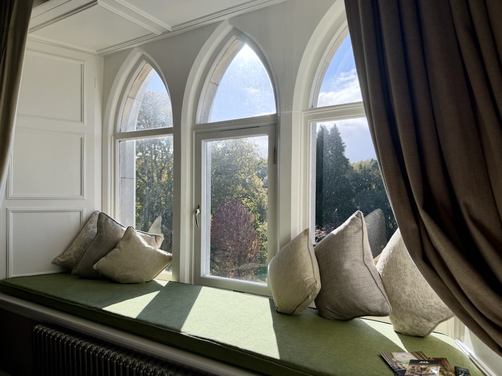 Cozy window seat with plush cushions and a view of the colorful garden at Cabra Castle in Ireland.