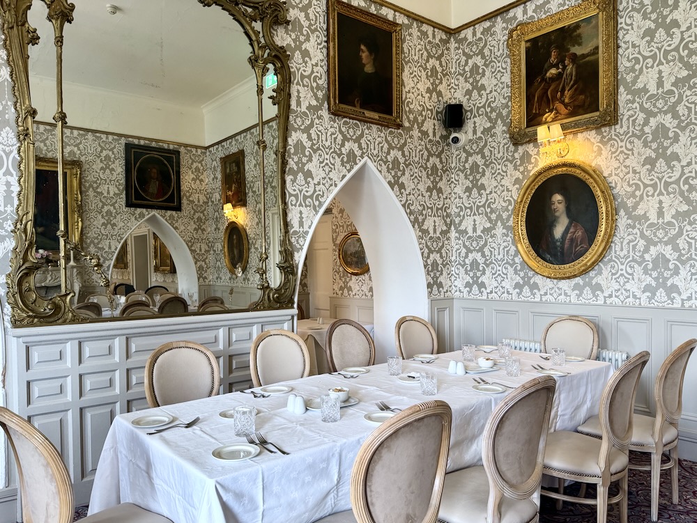 Elegant dining setting at Cabra Castle, featuring a white table, fine china, and vintage portraits on patterned wallpaper.
