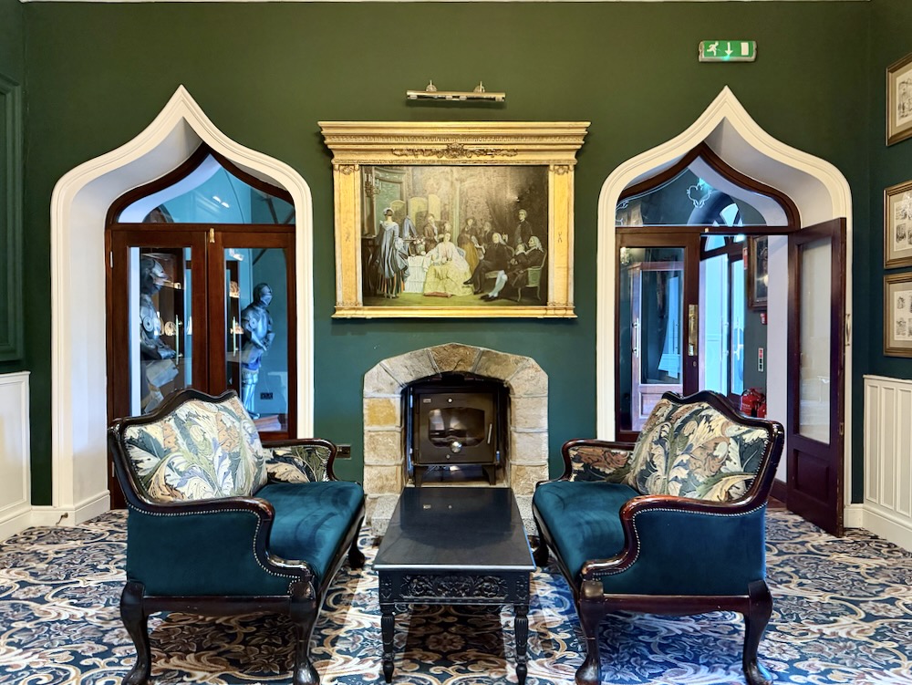 Elegant seating area in Cabra Castle featuring plush chairs, a fireplace, and a vintage painting on a dark green wall.