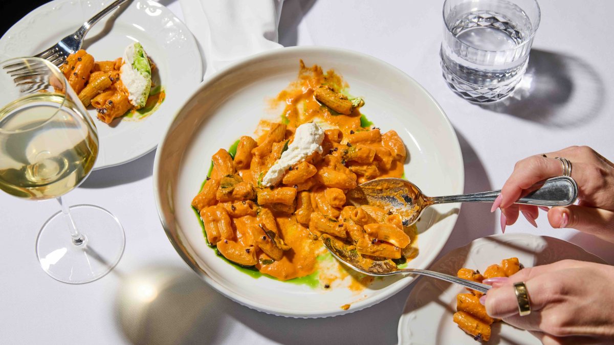 Spicy rigatoni garnished with fresh ricotta, served with a glass of white wine on a table set for dinner.