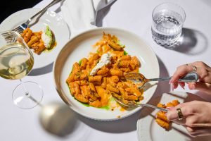 Spicy rigatoni garnished with fresh ricotta, served with a glass of white wine on a table set for dinner.