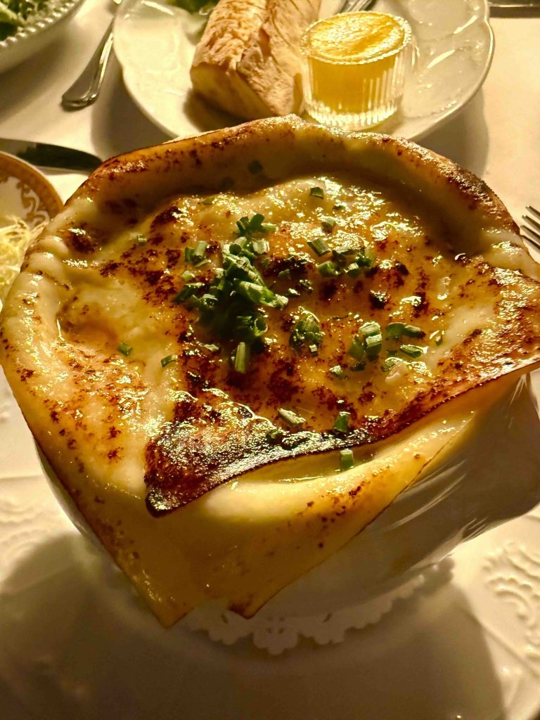 Rich onion soup topped with melted cheese and sprinkled with fresh chives, served with bread and a side of butter.