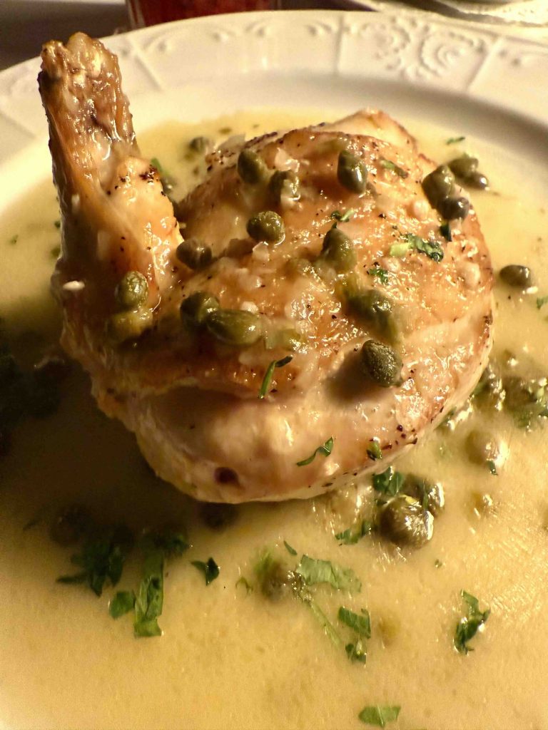 Crispy chicken piccata topped with capers and served in a light lemon sauce, garnished with fresh herbs.