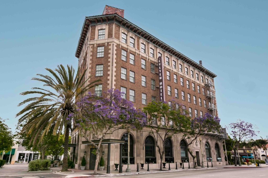 The Culver Hotel with palm trees and purple flowers, evoking Old Hollywood charm in a modern setting.