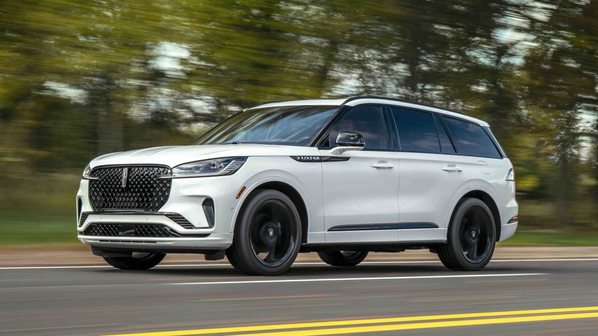 2026 Lincoln Aviator driving on a tree-lined road, showcasing its luxury design and advanced technology features.