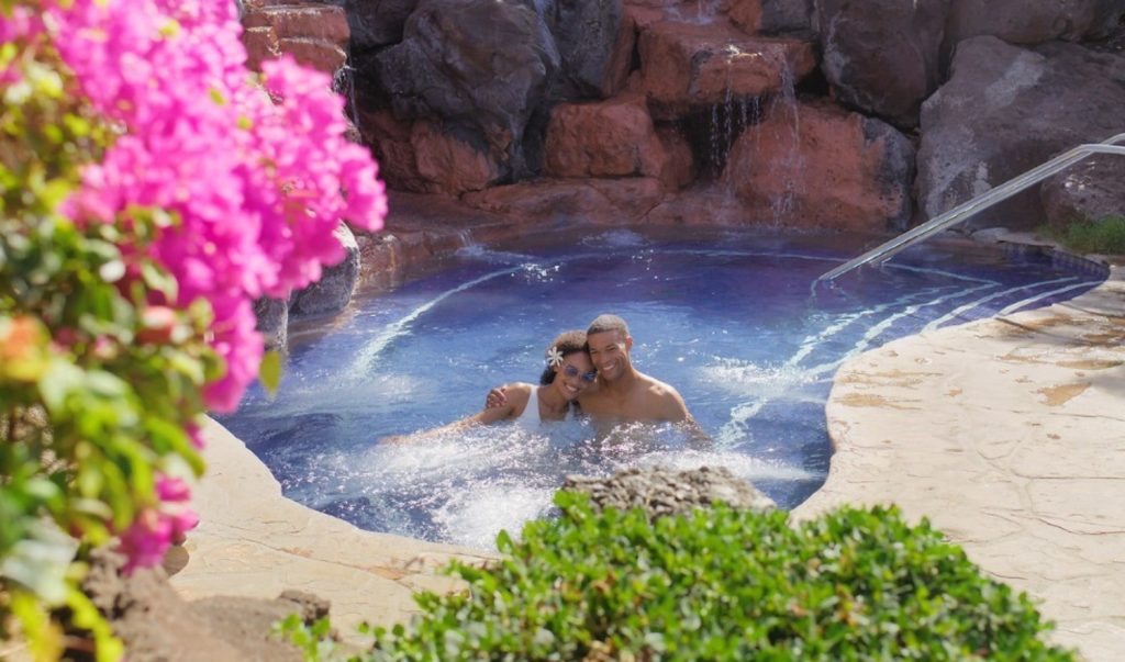 A couple enjoys a romantic moment together in a resort spa, surrounded by vibrant flowers and an inviting atmosphere.