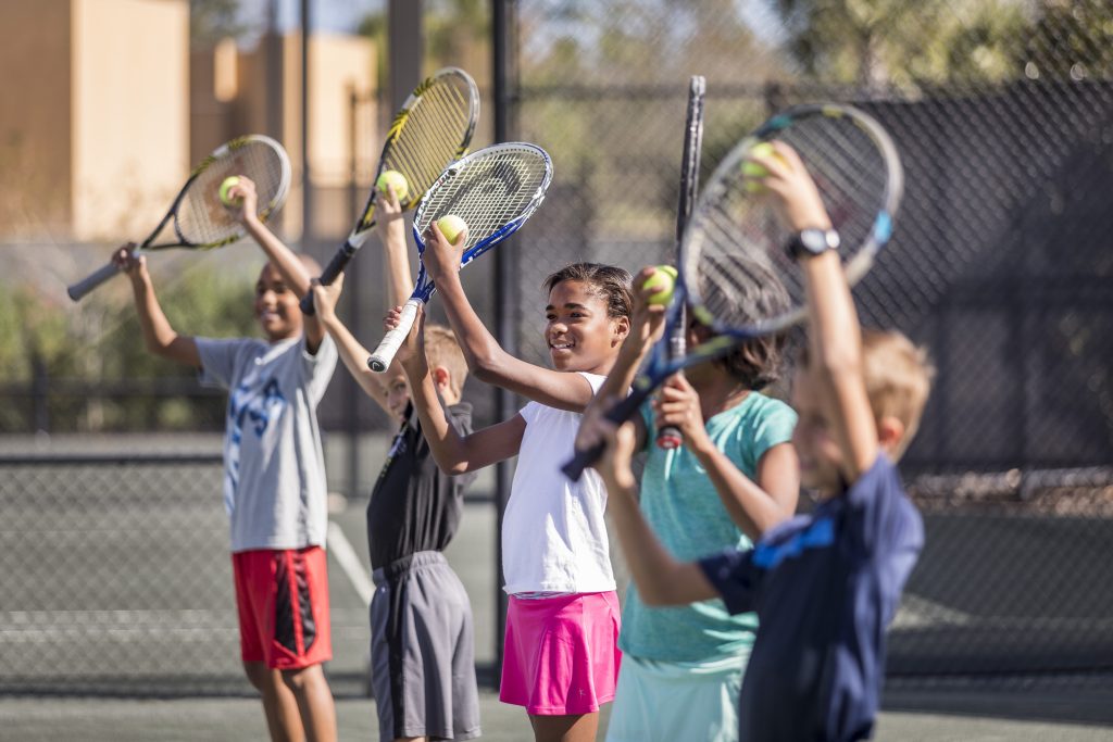 Children participate in a tennis camp at Four Seasons Resort Nevis, happily holding rackets and tennis balls.