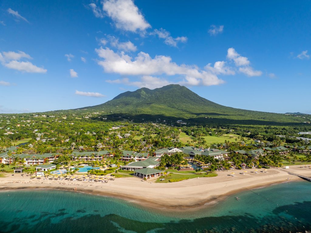 Aerial view of Four Seasons Resort Nevis with lush green mountains and a serene beach showcasing a tennis camp for kids.