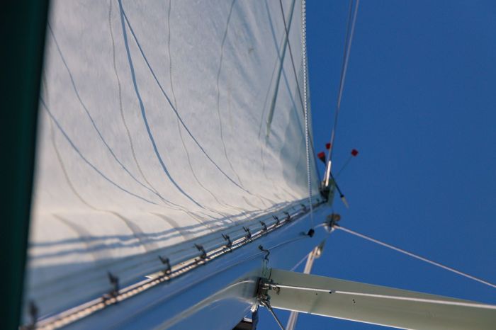 Sailcloth material is stretched upward against a clear blue sky, showcasing its texture and structural support.