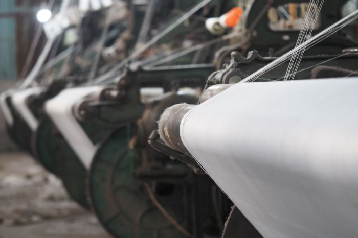 Sailcloth production machinery with spools of fabric being processed in a manufacturing facility.