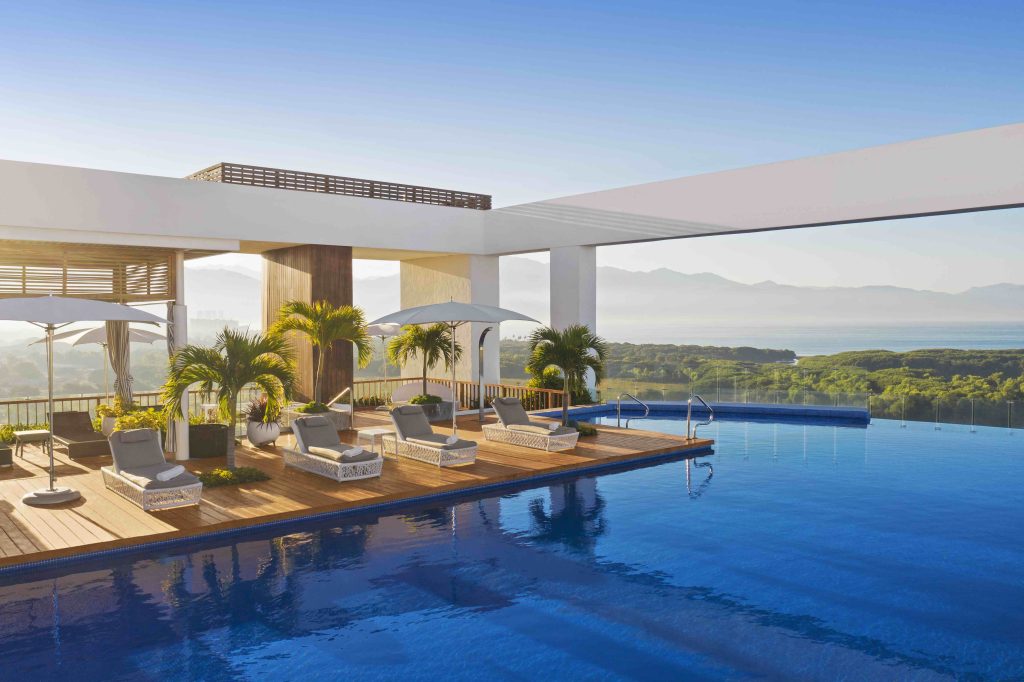 Luxury poolside area at VidantaWorld Nuevo Vallarta with loungers, umbrellas, and scenic views of hills and ocean.