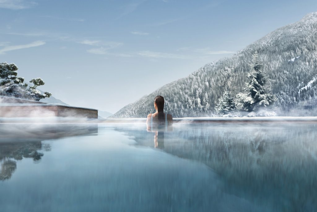A tranquil outdoor spa surrounded by snow-capped mountains, with a person relaxing in the warm water.