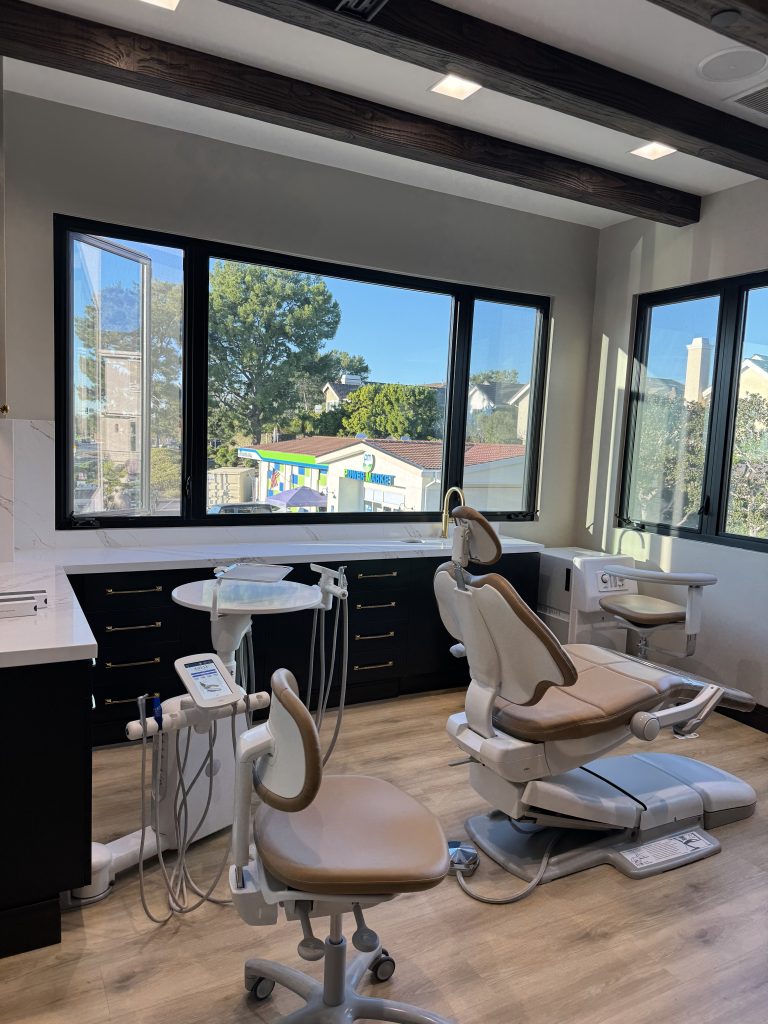 Modern aesthetic treatment room featuring dental chairs, equipment, and large windows with a view of the outdoors.