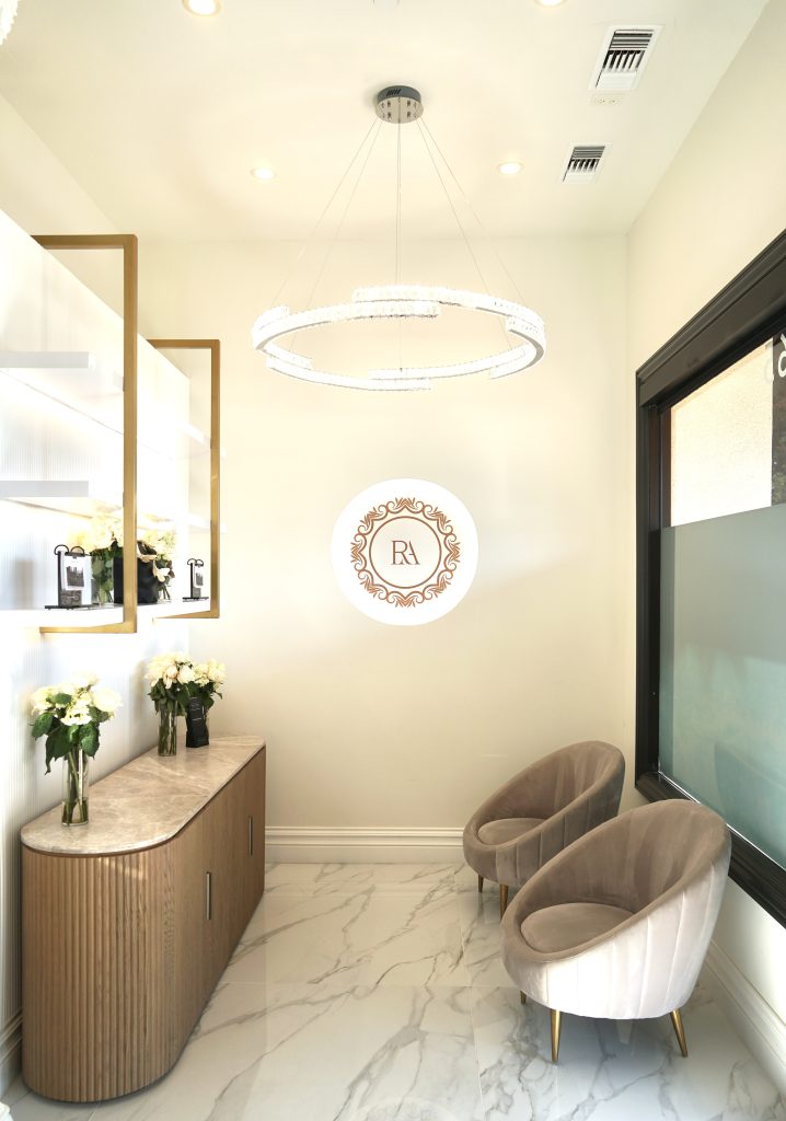 Modern aesthetic treatment room featuring a circular chandelier, elegant seating, and floral decor against a sleek interior design.