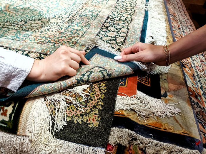 Two hands inspecting the intricate details of an antique Persian rug, highlighting its rich patterns and textures.