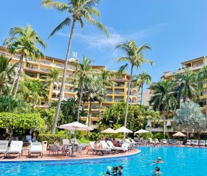 Resort pool surrounded by palm trees, lounge chairs, and vibrant greenery at the Velas Resorts in Mexico.