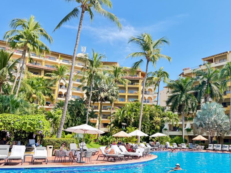 Resort pool surrounded by palm trees, lounge chairs, and vibrant greenery at the Velas Resorts in Mexico.